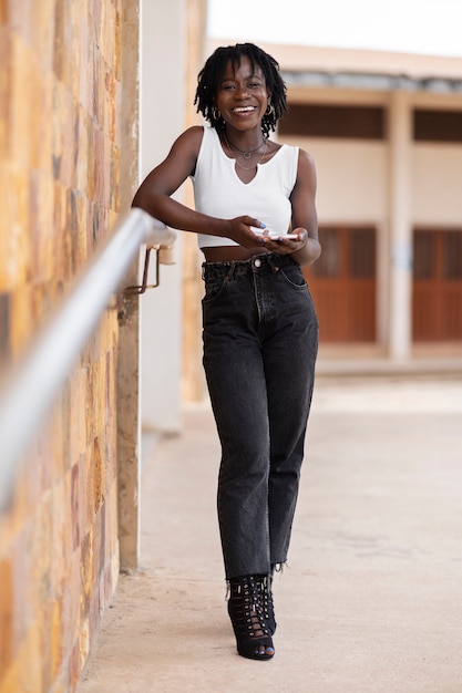 Portret van een jonge vrouw met afro-dreadlocks die smartphone buitenshuis gebruikt