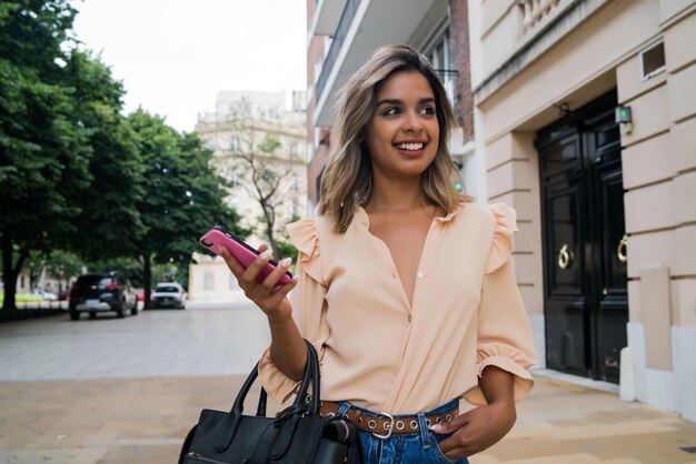 Portret van een jonge vrouw met behulp van haar mobiele telefoon tijdens het wandelen buiten op straat