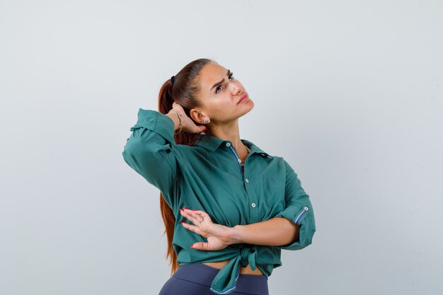 Portret van een jonge vrouw met de hand achter het hoofd, omhoog kijkend in een groen shirt en peinzend vooraanzicht