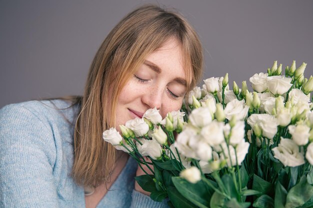 Portret van een jonge vrouw met een boeket rozen op een grijze achtergrond