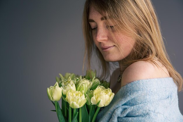 Portret van een jonge vrouw met een boeket tulpen op een grijze achtergrond