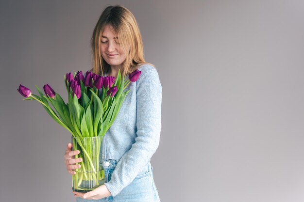 Portret van een jonge vrouw met een boeket tulpen op een grijze achtergrond