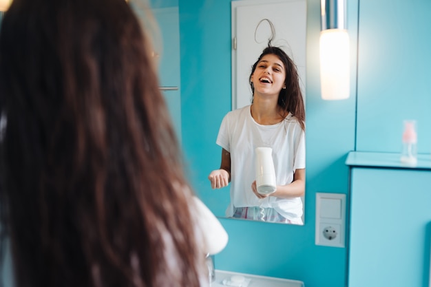 Portret van een jonge vrouw met een haardroger in de badkamer.