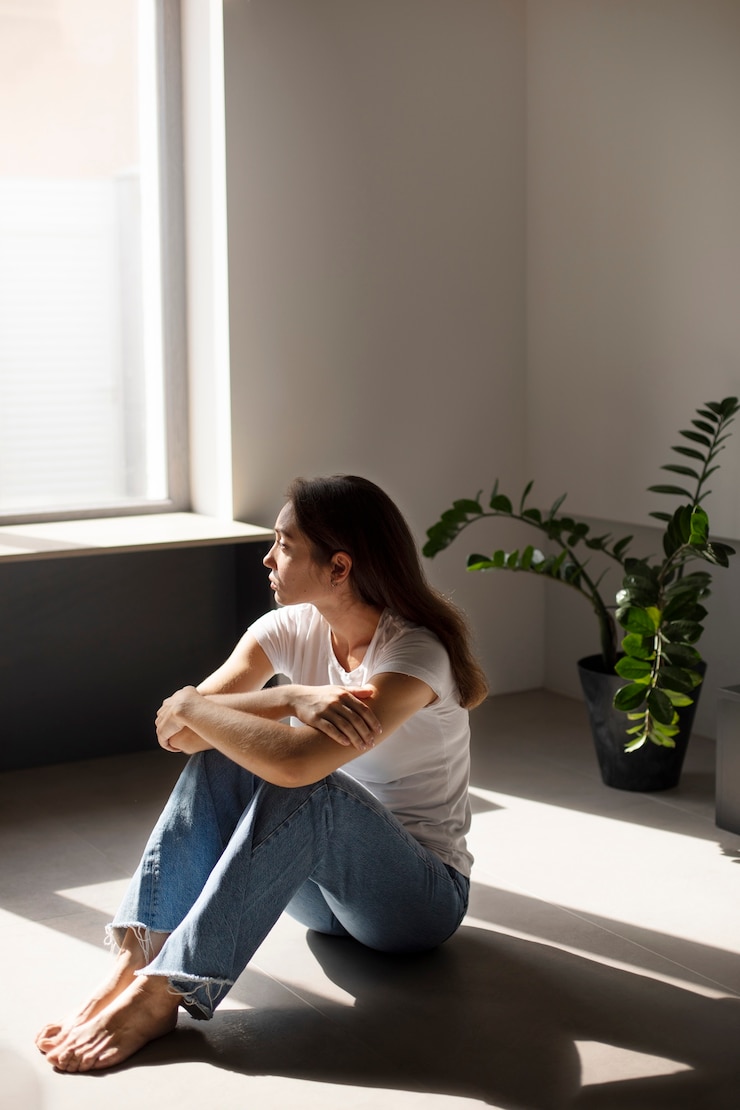 Gratis Foto portret van een jonge vrouw met een laag zelfbeeld die thuis bij het raam zit