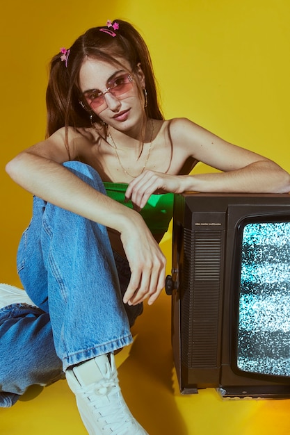 Portret van een jonge vrouw met een modestijl uit de jaren 2000, poserend met tv