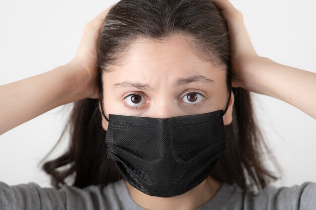 Portret van een jonge vrouw met een zwart gezichtsmasker die haar hoofd vasthoudt.