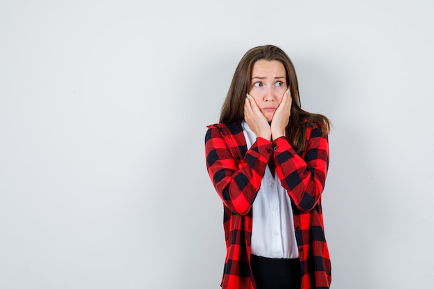 Portret van een jonge vrouw met handen op de wangen in vrijetijdskleding en een opgewonden vooraanzicht