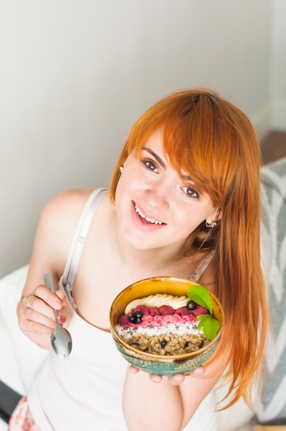 Portret van een jonge vrouw met kom met banaan; muesli en verse bessen