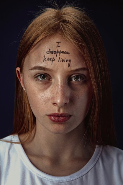 Portret van een jonge vrouw met psychische problemen. De afbeelding van een tatoeage op het voorhoofd met de woorden ik verdwijn-blijf leven.