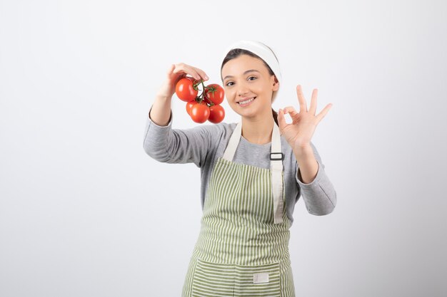 Portret van een jonge vrouw met rode tomaten over een witte muur