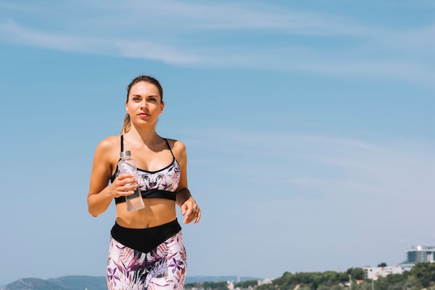 Portret van een jonge vrouw met waterfles in de hand joggen