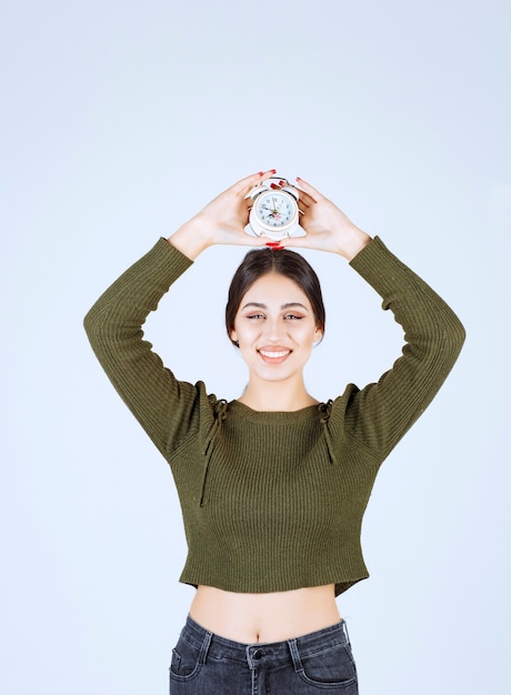 Portret van een jonge vrouw met wekker op witte achtergrond.