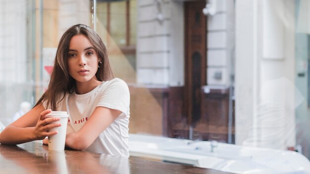 Portret van een jonge vrouw zitten in cafe met afhaalmaaltijden koffie kopje in de hand kijken naar de camera