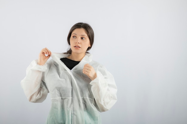 Portret van een jonge vrouwelijke arts-wetenschapper in defensieve laboratoriumjas die wegkijkt.