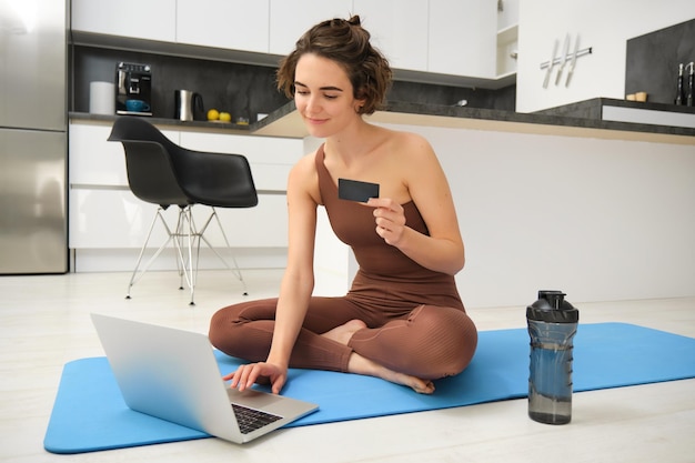 Gratis foto portret van een jonge vrouwelijke atletische yoga-meid die voor online lessen betaalt en training op afstand koopt met