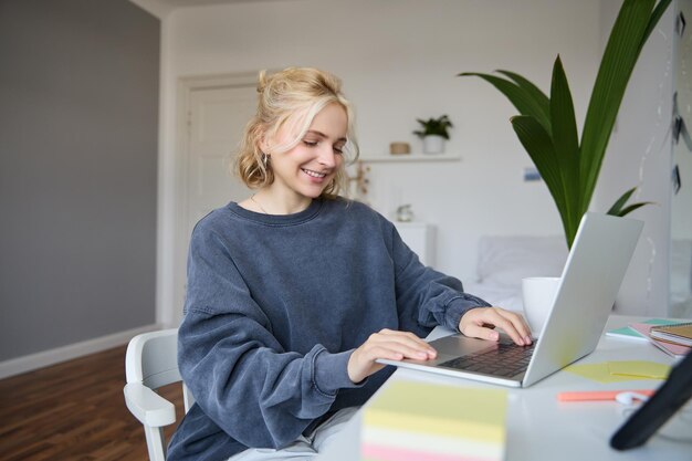 Portret van een jonge vrouwelijke student die thuis studeert op afstandsonderwijs en op een laptop schrijft