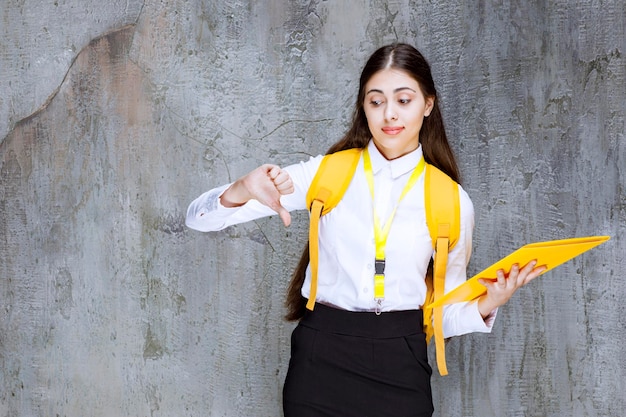 Portret van een jonge vrouwelijke student met een geel notitieboekje die duimen naar beneden geeft. Hoge kwaliteit foto