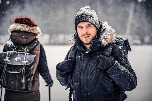 Portret van een jonge wandelaar met een rugzak die met zijn vriendin door een winterbos loopt