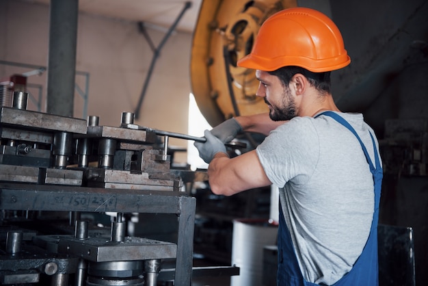 Portret van een jonge werknemer in een harde hoed bij een grote metaalbewerkingsfabriek.