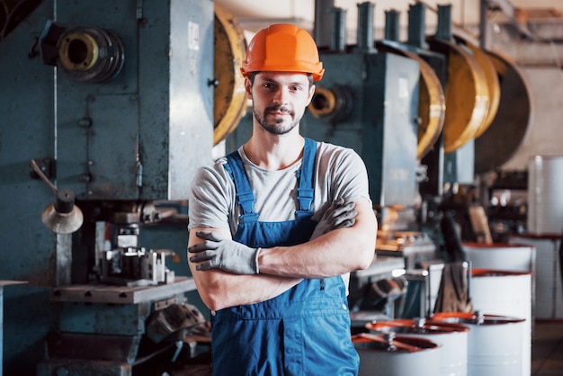 Portret van een jonge werknemer in een harde hoed bij een grote metaalbewerkingsfabriek.