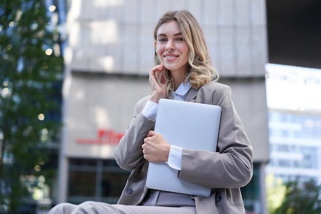 Portret van een jonge zakelijke vrouw die haar laptop vasthoudt en glimlachend naar haar werk gaat met een professional