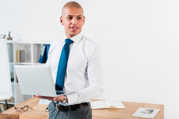 Portret van een jonge zakenman die in hand het open laptop weg kijken houdt