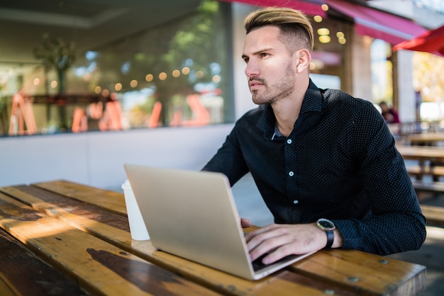 Portret van een jonge zakenman die op zijn laptop werkt terwijl hij in een coffeeshop zit. Technologie en bedrijfsconcept.