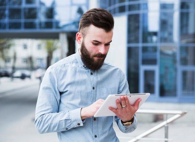 Portret van een jonge zakenman die zich buiten het bureaugebouw bevindt dat digitale tablet gebruikt
