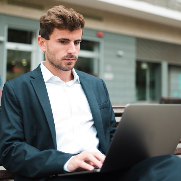 Portret van een jonge zakenmanzitting die in openlucht laptop met behulp van