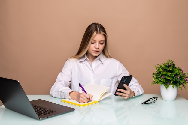 Portret van een jonge zakenvrouw die de telefoon gebruikt en opmerkt in een notitieboekje op kantoor