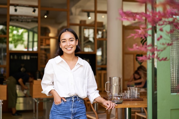 Portret van een jonge zakenvrouw in haar eigen cafémanager die bij de ingang staat en je posi uitnodigt