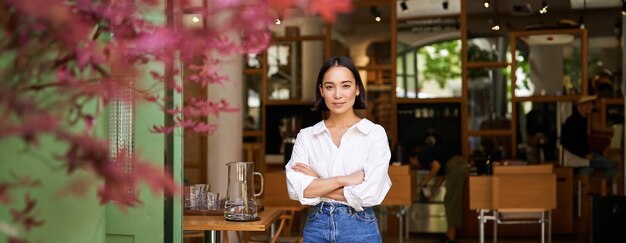 Portret van een jonge zakenvrouw in haar eigen cafémanager die bij de ingang staat en u uitnodigt