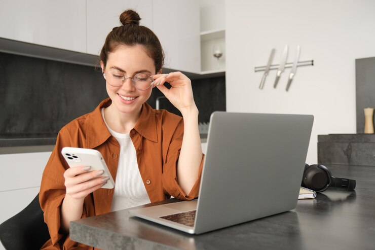 Gratis Foto portret van een jonge zelfstandige vrouw die klanten op een smartphone beantwoordt met een laptop om te controleren