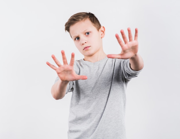 Portret van een jongen die aan camera kijkt die eindegebaar maakt die op witte achtergrond wordt geïsoleerd