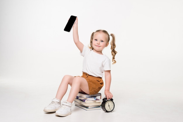 Portret van een klein de telefoonschermzitting van de meisjesholding op een stapel boeken.