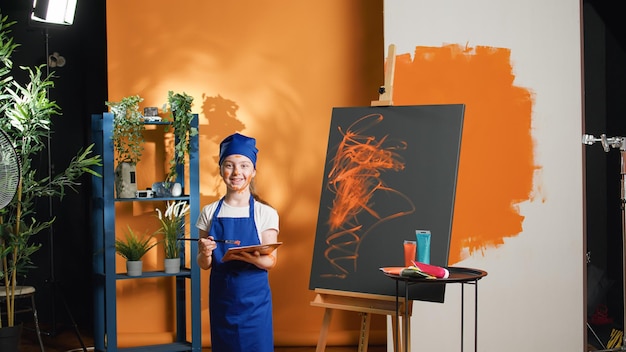 Gratis foto portret van een klein kind dat kunstwerkontwerp op canvas schildert, met artistiek aquarelpalet en penseel. jong meisje leren meesterwerk te schilderen met waterverf en penseel, creatieve vaardigheden.