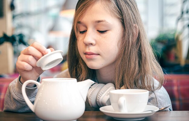 Portret van een klein meisje in een café met een theepot en een kopje