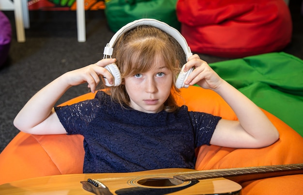 Portret van een klein meisje in een koptelefoon en met een gitaar tijdens het leren van muziek