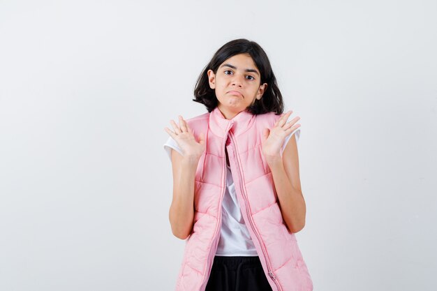 Portret van een klein meisje in wit t-shirt en puffervest dat handen opheft