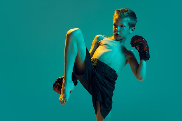 Portret van een kleine jongen in handschoenen die thaiboksen traint op een groene studioachtergrond in neonlicht