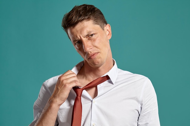 Portret van een knappe donkerbruine man met bruine ogen, gekleed in een klassiek wit overhemd en een rode stropdas, die hij ontspant. Hij poseert in een studio tegen een blauwe achtergrond. Concept van gebaren an