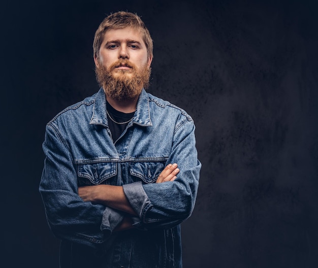 Portret van een knappe hipster kerel gekleed in jeans jasje poseren met gekruiste armen. Geïsoleerd op een donkere achtergrond.