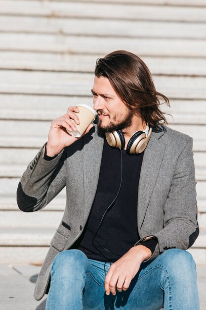 Portret van een knappe jonge man met een hoofdtelefoon rond zijn nek drinken afhaalmaaltijden koffie