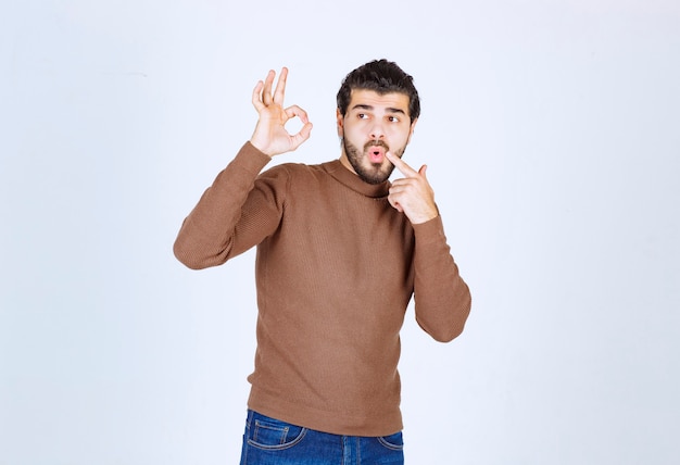 Portret van een knappe jongeman die een goed gebaar toont dat op de witte achtergrond wordt geïsoleerd. Hoge kwaliteit foto