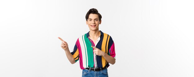Portret van een knappe jongeman in stijlvolle kleding die met de vingers naar links wijst en lacht met advertenties