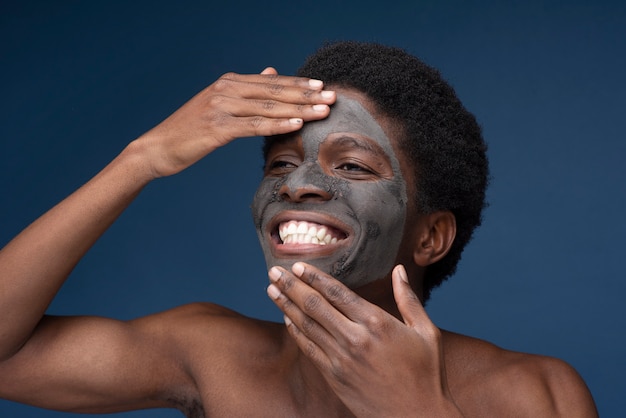 Gratis foto portret van een knappe man die lacht met een houtskoolmasker op zijn gezicht