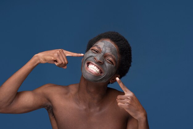 Gratis foto portret van een knappe man die naar het houtskoolmasker op zijn gezicht wijst