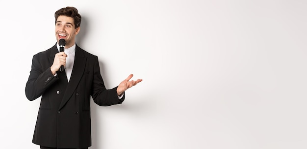 Gratis foto portret van een knappe man in een zwart pak die een lied zingt terwijl hij een microfoon vasthoudt en staande een toespraak houdt