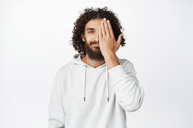 Portret van een knappe man uit het Midden-Pasen met een baard die de helft van het gezicht bedekt en lacht en kijkt met één oog naar de witte achtergrond van de camera