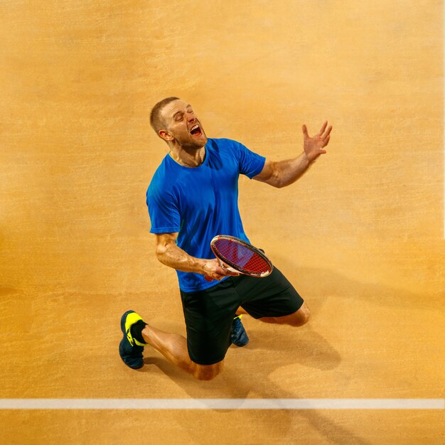 Portret van een knappe mannelijke tennisser die zijn succes op een hofmuur viert